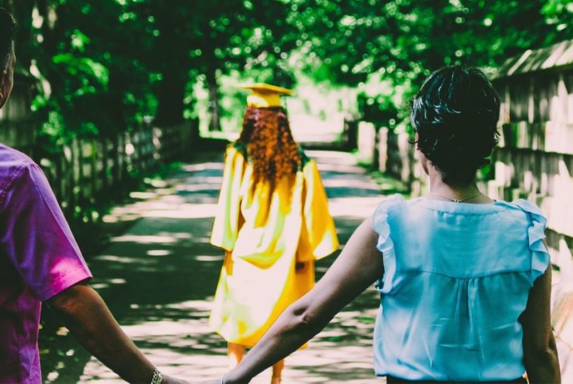 Parents holding hands as daughter walks away in graduation cap and gown