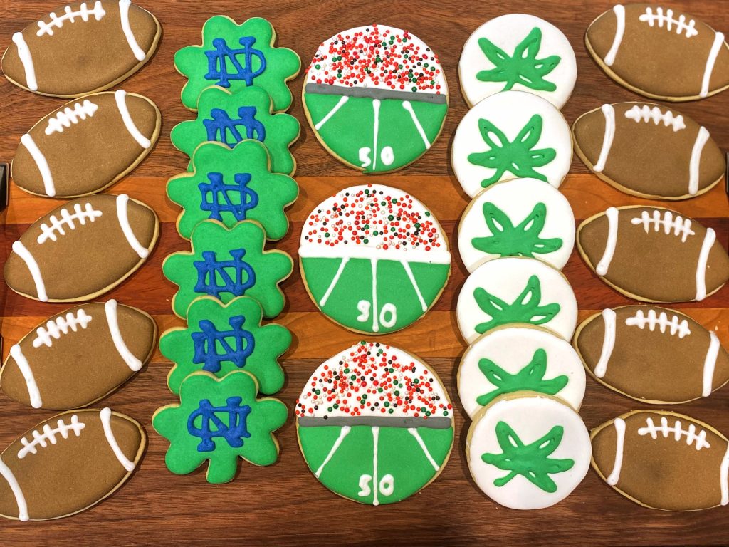 Tray of football cookies, with football field, Ohio State Buckeye leaf stickers and Notre Dame shamrocks.