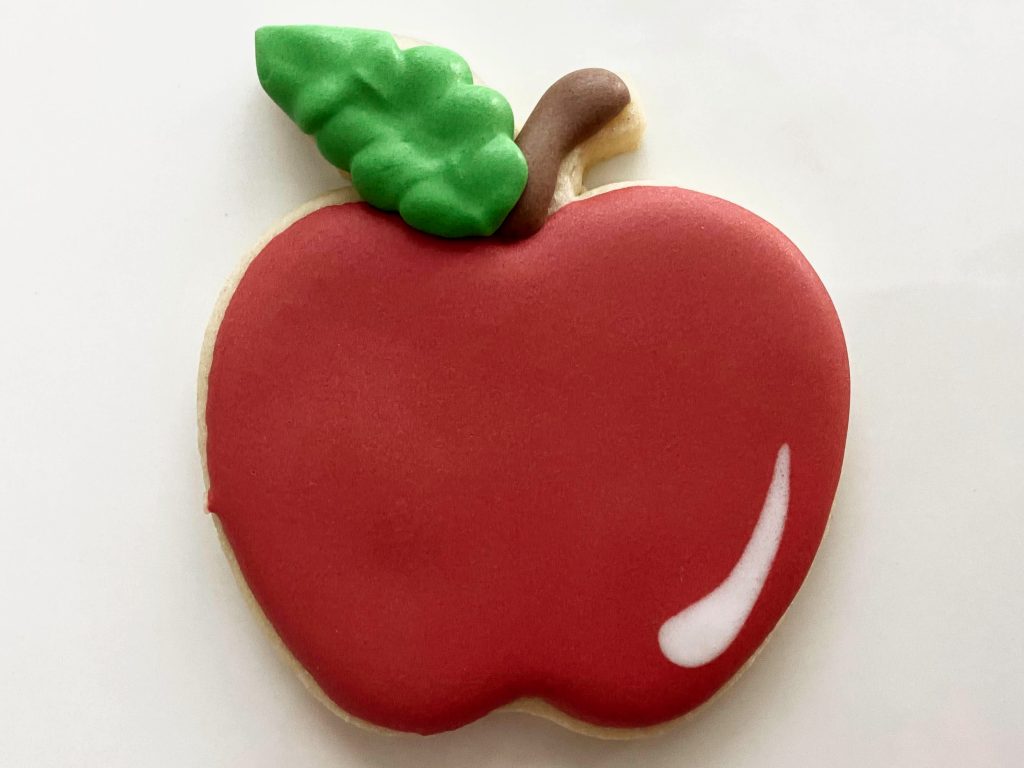 Apple cookie with textured green leaf, brown stem and red apple.