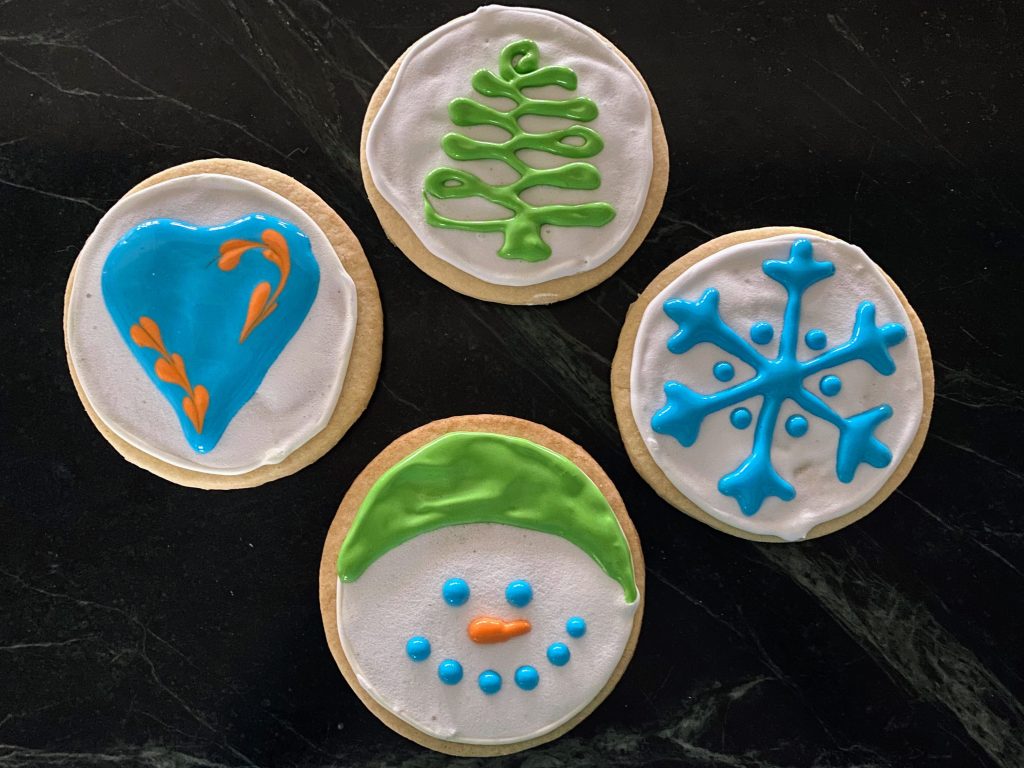 Round cookies -- snowman, Christmas tree, heart and snowflake -- on a black background. These are my first attempt at decorated sugar cookies