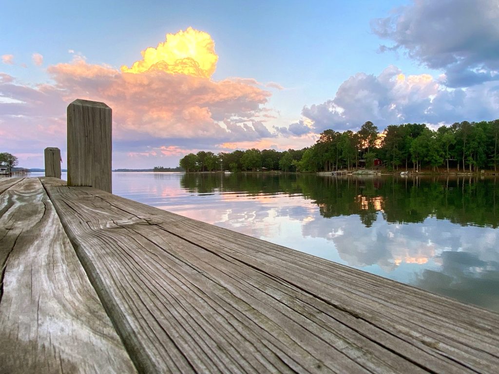 dock boards in foreground with lake behind reflecting the clouds and far shoreline.