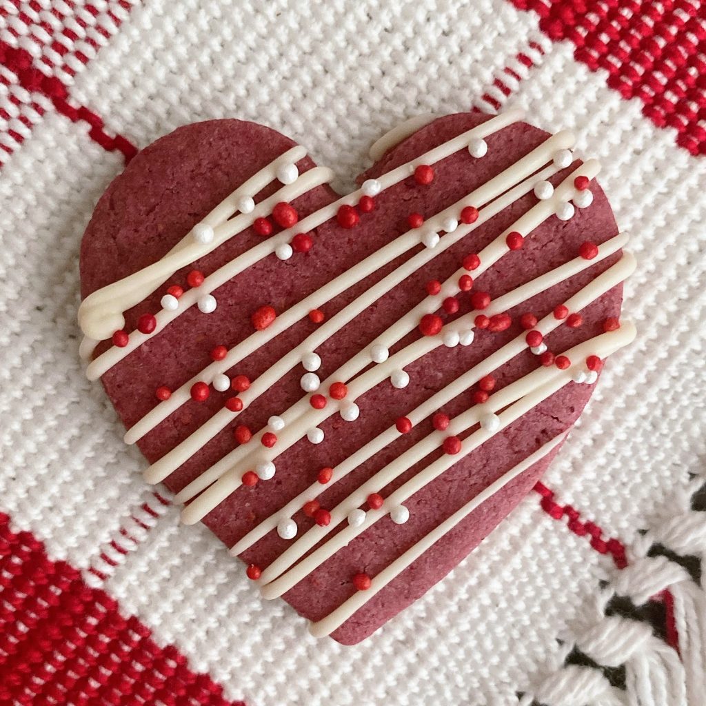 Raspberry cookie with white chocolate drizzle on a red and white background