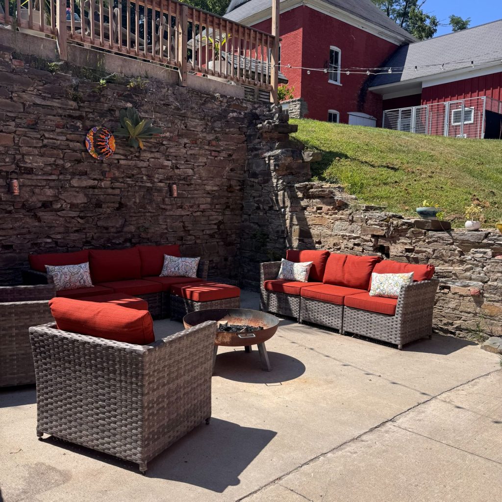 Fire pit lounge area, with orange cushioned wicker seating, fire pit and stone walls.